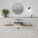 Bestile Blesle White 60x60- gresowa płytka imitująca jasne lastryko z kolorowym wyraźnym oczkiem na ścianie jasnej łazienki. Okrągłe lustro, podwieszany drewniany blat, czarna armatura podtynkowa, czarna umywalka nablatowa