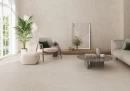 Ecoceramic Babilon Bone Matt 60x120- gresowa płytka imitująca beżowy beton o matowym wykończeniu na ścianach i podłodze salonu. Szara kanapa, fotel na drewnianej ramie, okrągły stolik ze szklanym blatem.