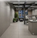 Nowoczesna aranżacja wnętrza komercyjnego w stylu industrialnym z szarymi płytkami gresowymi Marazzi SistemT Graniti Grigio Scuro Rock M7K0 na podłodze i ścianie. W tle strefa warsztatowa, skórzana kanapa, ceglana ściana oraz oświetlenie techniczne.