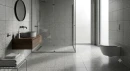Nowoczesna łazienka z kwadratowymi płytkami gresowymi Marazzi SistemT Graniti Medio Grigio 20x20 M7K7 imitującymi beton na ścianach i podłodze. W aranżacji kabina walk-in, drewniana szafka z okrągłą umywalką oraz wisząca miska WC.