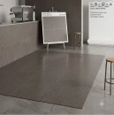 Wizualizacja kawiarni z ciemnoszarymi, kwadratowymi płytkami Marazzi SistemT Graniti Grigio Scuro 20x20 cm M7K6. Matowe kafle o strukturze granitu pokrywają podłogę, ścianę i ladę barową. W tle stoi sztaluga z próbnikami oraz hoker.