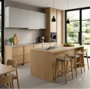 Nowoczesna drewniana kuchnia. Na podłodze jasnoszare płytki Marazzi SistemT - Graniti Grigio Chiaro 20x20 cm M642 imitujące beton. W centrum drewniana wyspa z hokerami. Duże okna z widokiem na ogród wpuszczają naturalne światło.