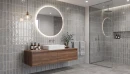 Gayafores Deco River Grey 32x62,5- szara, dekoracyjna płytka ścienna w połysku na ścianach łazienki. Podwieszana ciemna drewniana szafka łazienkowa. Biała umywalka nablatowa. Okrągłe lustro z podświetleniem LED.