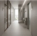 Płytki gresowe Marazzi SistemT Graniti Grigio Chiaro Diamond 20x20 cm MHX0 z wypukłą, geometryczną fakturą pokrywają ściany i podłogę nowoczesnego korytarza prowadzącego do toalet. Wejścia zdobią szklane i metalowe drzwi.