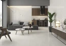 Prissmacer Sun White Pulido 120x120- klasyczny kamień w jasnoszarym kolorze i połysku. na ścianach i podłodze otwartego salonu połączonego z kuchnią. Ciemna zabudowa kuchenna pasująca do stojącej w salonie szafki. Grafitowe obicia mebli w salonie.