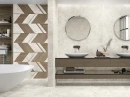 Porcelanite Dos Rapolano White 100x100- gresowa płytka imitująca surowy kamień w szarym kolorze na ścianach i podłodze łazienki. Drewniane podwieszane szafki łazienkowe. Drewniany lamelowany dekor na ścianie przy wannie wolnostojącej.