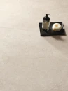 Ergon Matera Stone Neutra Beige Silktech 60x120 EN53- gresowa płytka imitująca beżowy kamień z przebarwieniami na podłodze salonu. Czarna prostokątna podstawka z kosmetykami.
