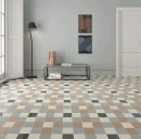 Jasne wnętrze z podłogą w geometryczny wzór, wykorzystującą błyszczące, ciemne płytki WOW Bits Square Storm Gloss 11,6x11,6 cm (133018). W tle jasnoszara ściana, czarny metalowy stolik ze szklanym blatem, wysoka lampa i białe drzwi.