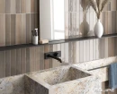 Equipe Isola Castle Rock 5x30- wielokolorowa płytka ścienna w odcieniach brązu i szarości na ścianie łazienki. Kamienna ściana razem z kwadratową umywalką. Czarna podtynkowa armatura łazienkowa, prostokątne lustro w czarnej ramce.