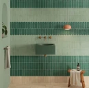 Aranżacja łazienki z umywalką i mosiężną baterią. Ściany wyłożono pionowo błyszczącymi płytkami WOW Casablanca Basil Gloss 5x15 135381 w kolorze głębokiej zieleni, tworząc pasy z jasnymi, miętowymi płytkami.