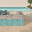 Widok na strefę wypoczynkową przy basenie na tarasie. Pionowe boki kanapy i obrzeże basenu są wyłożone błyszczącymi płytkami WOW Casablanca O Water Gloss 5x15 135385 w odcieniu morskim. Na kanapie widać poduszki i książkę.