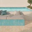 Strefa wypoczynkowa przy basenie z posadzką z beżowych, owalnych płytek WOW Casablanca O Adobe Gloss 5x15 cm 135390. Obok stoi wbudowane siedzisko obłożone turkusowymi kafelkami, z miękkim materacem, poduszkami i otwartą książką.