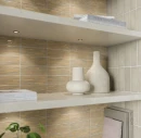Zbliżenie na betonowe półki z dekoracjami, w tym wazonami i książkami, jak "Parisian Interiors". Ściana w tle wyłożona jest teksturowanymi, prążkowanymi, błyszczącymi płytkami WOW Casablanca Comb Ash Gloss 5x15 cm (135394) w odcieniach szarości i beżu.