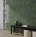 Eleganckie wnętrze ze ścianą z ciemnozielonych, błyszczących płytek WOW Colour Notes Fennel Gloss 4x12,5 (132962) ułożonych pionowo. W aranżacji znajduje się czarna drewniana ławka z wazonami, pufy i biały regał.