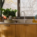 Kuchnia z oknem przy blacie roboczym, drewnianymi frontami szafek, wpuszczanym zlewozmywakiem oraz białą baterią kuchenną stojącą Omnires SWITCH - SW9057WM