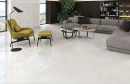 Emigres Global Blanco Lappato 60x60 gresowa płytka imitująca kamień ze skrzącą się powierzchnią  na podłodze salonu. Szara kanapa, musztardowy fotel z podnóżkiem na czarnych nogach.