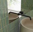 Zielone, błyszczące płytki WOW Colour Notes Bars Fennel 4x12,5 133157 ułożone pionowo na ścianie w nowoczesnej łazience. W aranżacji ze strukturalną ceramiką widoczna jest czarna bateria podtynkowa oraz beżowa umywalka.