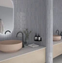 Jasnofioletowe płytki WOW Colour Bars Viola Gloss 4x12,5 cm 133164 na zaokrąglonej ścianie w łazience. Modernistyczna aranżacja z pudroworóżową umywalką nablatową, czarną baterią, drewnianą szafką i podświetlanym lustrem.