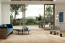 Coem Aquitaine Beige Naturale Modulo AQ2MD gresowa płytka podłogowa imitująca beżowy kamień  na podłodze salonu. Duże rozsuwane okno z wyjściem na taras. Drewniana kanapa z niebieskim obiciem.