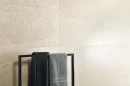 Coem Blendstone Ivory Lucidato 60x60 BL601LR gresowa płytka imitująca jasny beżowy kamień z jasnymi żyłami na ścianie łazienki. Czarny metalowy stojak/wieszak na ręczniki.
