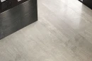 Coem Blendstone Grey Lucidato 60x60 BL603LR szara gresowa płytka imitująca jasny kamień z jasnymi żyłami i przebarwieniami  na podłodze holu hotelowego. Grafitowy kamień na ladzie i ścianach holu. Brązowy blat.