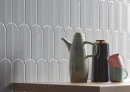 Ściana z płytkami o unikalnym kształcie rybiej łuski w chłodnym, perłowo-białym odcieniu Cifre Alma Scale Pearl Brillo 8x21,5, z drewnianym blatem i ceramiką w kolorze pastelowym