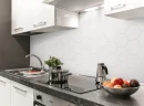 Kuchnia z białymi szafkami, ciemnym marmurowym blatem, chromowaną armaturą oraz białą mozaiką ścienną w kształcie heksagonów Ceramik Studio Heksagon White Mat 36x25