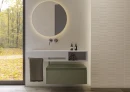 Beżowa łazienka ze ścianą z płytek Cifre Alure Ivory Mate Rc Pb 30x75 RC PB imitującymi beton, srebrną armaturą, okrągłym podświetlanym lustrem, dużym oknem, białym podwieszanym blatem, podłogą w kolorze drewna.
