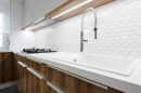 Kuchnia z drewnianymi szafkami, białym blatem, chromowaną baterią i białą mozaiką ścienną w kształcie rombów Ceramik Studio Daring Snow 30,5x30,8