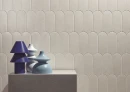 Ściana z beżowawymi płytkami pochodzenia hiszpańskiego Cifre Alure Scale Ivory Mate 8x21,5 w kształcie rybiej łuski, z dekoracyjną konsolą i niebieskimi wazonami w kolorze głębokiego indygo, perłowej bieli i błękitu.