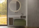 Łazienka z szarymi hiszpańskimi płytami imitującymi beton Cifre Alure Plomb Mate Rc Pb 30x75 RC PB, białą podwieszaną umywalką, otwartą półką na ręczniki, wiszącą szafką, podtynkową chromowaną baterią umywalkową, okrągłym podświetlanym lustrem.