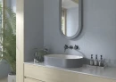 Nowoczesna łazienka, z niebieskimi płytkami imitującymi beton Cifre Alure Aqua Mate Xs Pb 25x50 XS PB, niskim podwieszanym blatem, drewnianymi frontami meblowymi, owalną umywalką nablatową, czarną armaturą ścienną, zaokrąglonym lustrem.