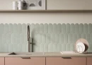 Ściana w kuchni z płytkami ściennymi, koloru zielonego, imitującymi beton Cifre Alure Scale Sage Mate 8x21,5, z jasnym drewnianym blatem, beżowym zlewem, pudroworóżowymi frontami szafek, wysoką baterią w odcieniu szczotkowanego złota.