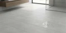 Łazienka z płytkami podłogowymi z Hiszpanii imitującymi beton, antypoślizgowymi, matowymi Cifre Alure Pearl Mate Sl Rc Antislip 60x120 SL RC, z kabiną walk-in, odpływem liniowym, podwieszaną szafką w kolorze jasnego drewna, z białym zlewem i dużym oknem.