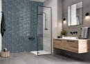 Łazienka z szarymi płytkami ścienno-podłogowymi, kabiną prysznicową z dekoracyjną niebieską mozaiką ułożoną w jodełkę Ceramik Studio Vibrant Blue, drewnianą wiszącą szafką oraz czarną armaturą