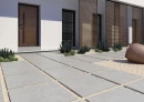 Strefa wejściowa z matowymi, tarasowymi płytkami imitującymi beton  Cifre Acron Pearl Mate Rc 20Mm Antislip 60x60 20MM, z drewnianymi drzwiami, białą elewacją, czarnymi ramami drzwi i okien, drewnianymi lamelami, z kaktusami i sukulentami.