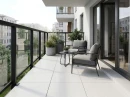 Balkon z białymi płytkami tarasowymi, antypoślizgowymi, imitującymi beton  Acron White Mate Rc 20Mm Antislip 60x60 20MM , z czarnymi ramami okiennymi,metalowo-szklaną balustradą, fotelami, stolikiem kawowym i roślinami.