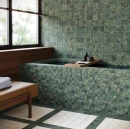 Elegancka łazienka z wanną obudowaną zielonymi płytkami ścienno-podłogowymi WOW Marble Pixel Green R11 15x15 cm (142012) o pikselowej strukturze. Obok podłoga w jasne i ciemne kwadratowe kafelki, okno oraz skórzana ławka.