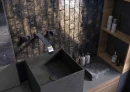 Ciemna łazienka z płytkami ściennymi, cegiełkami w połysku Cifre Ark Metal Brillo 6x25, z czarnym zlewem, srebrną armaturą, drewnianą otwartą szafką.