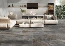 Salon z ciemnymi płytkami hiszpańskimi, imitującymi kamień Cifre Arven Dark Mate Sl Rc N-Plus 60x120 SL RC, z  dużą modułową jasną sofą w z plecionymi bokami, zestawiona z niskimi, z nowoczesnymi stolikami kawowymi, kominkiem.