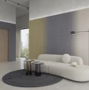 Nowoczesny salon z niebieskimi płytkami WOW Melange Sea 10,7x54,2 cm (132674) ułożonymi poziomo na ścianie w kompozycji z przejściem tonalnym. Eleganckie wnętrze z jasną sofą, szarym dywanem, szklanymi stolikami i czarną lampą podłogową