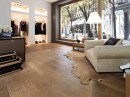 Wnętrze butiku z jasnym fotelem wypoczynkowym i płytkami drewnopodobnymi Porcelanosa Manhattan Cognac