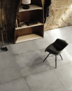 Aranżacja wnętrza w styli industrialnym z regałem, krzesłem i płytkami podłogowymi imitującymi beton Leonardo Ceramica Waterfront 90G