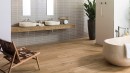 Łazienka z wanną wolnostojącą, umywalkami nablatowymi i brązowymi płytkami podłogowymi drewnopodobnymi Porcelanosa Delaware Natural